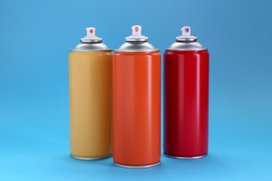 Photo of Three spray paint cans on light blue background