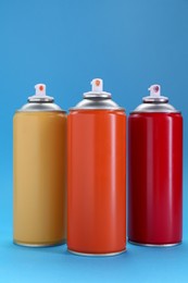 Photo of Three spray paint cans on light blue background