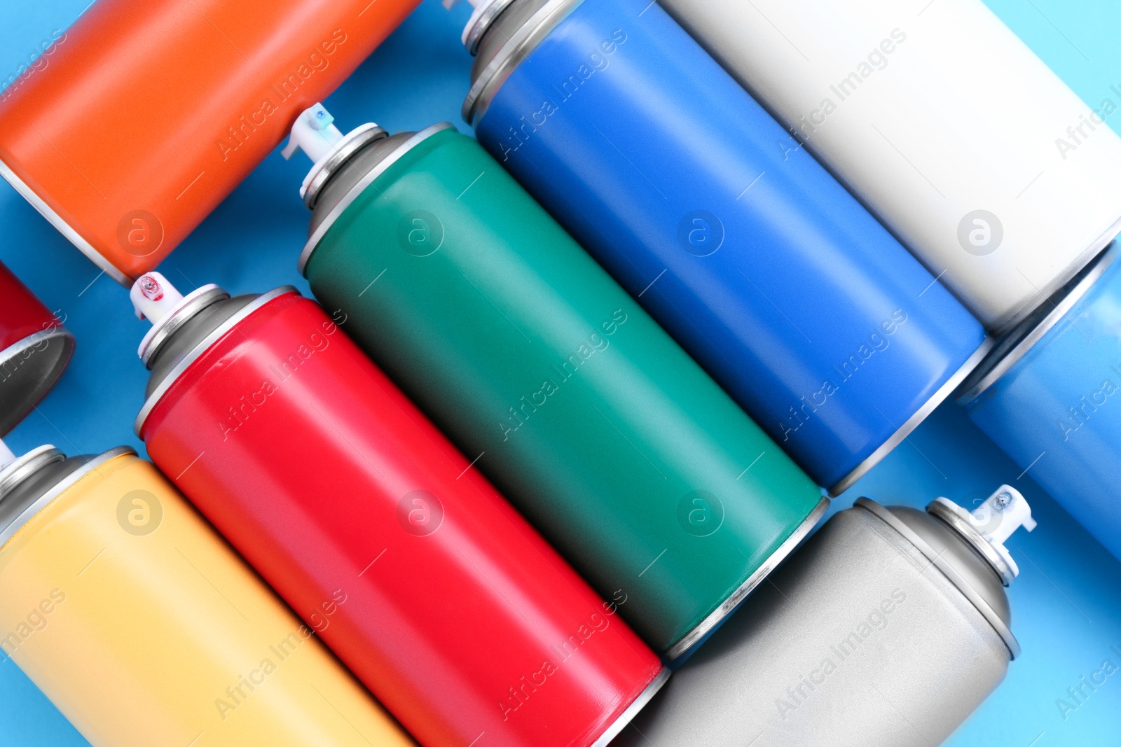 Photo of Many spray paint cans on light blue background, top view