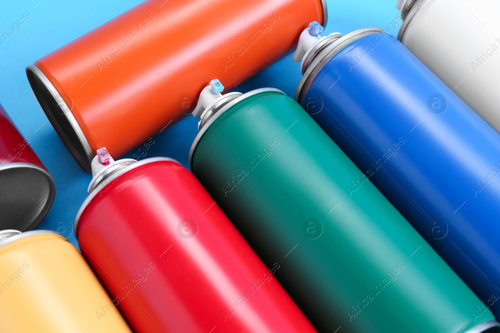 Photo of Many spray paint cans on light blue background, closeup