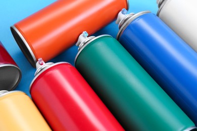 Photo of Many spray paint cans on light blue background, closeup