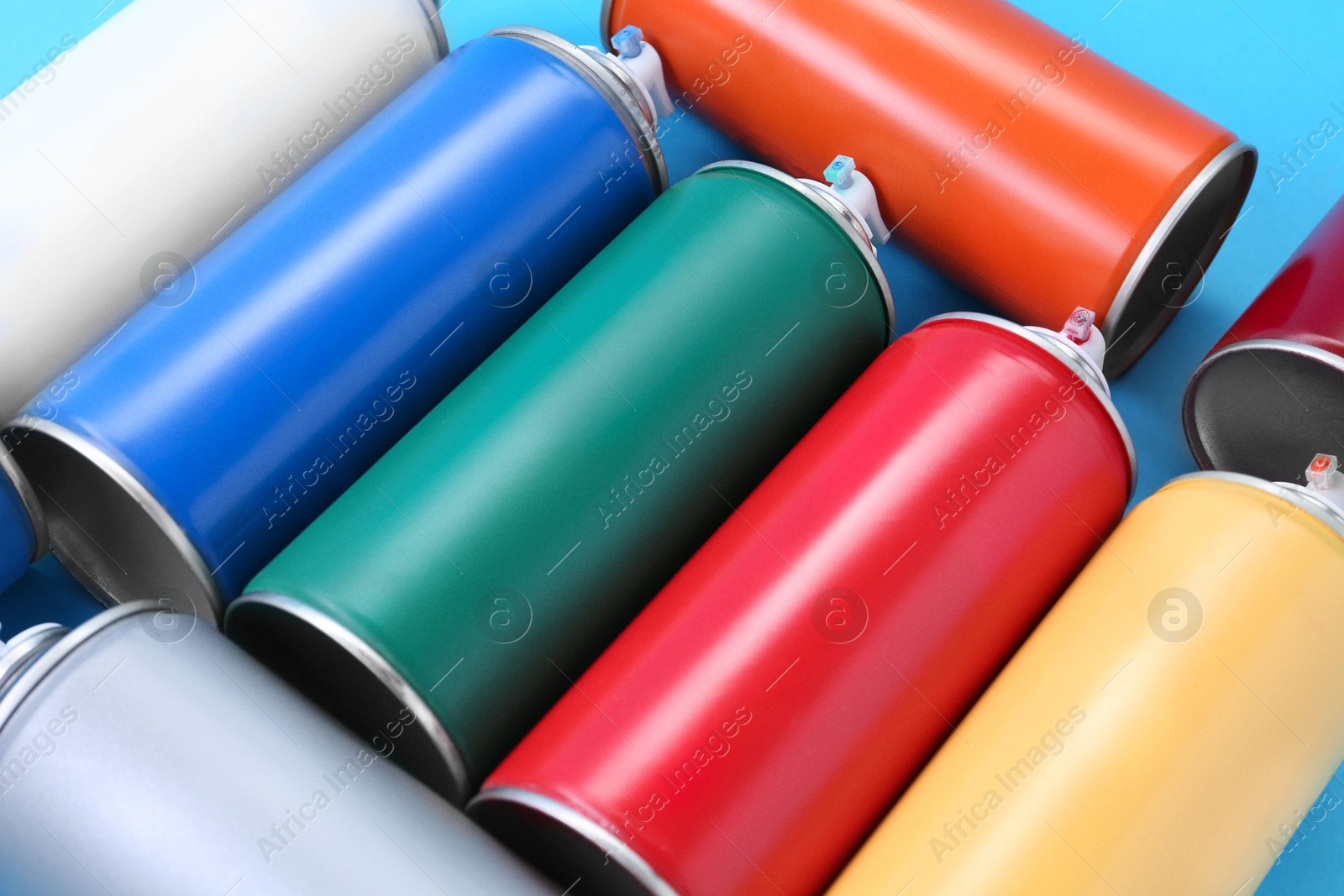 Photo of Many spray paint cans on light blue background, closeup