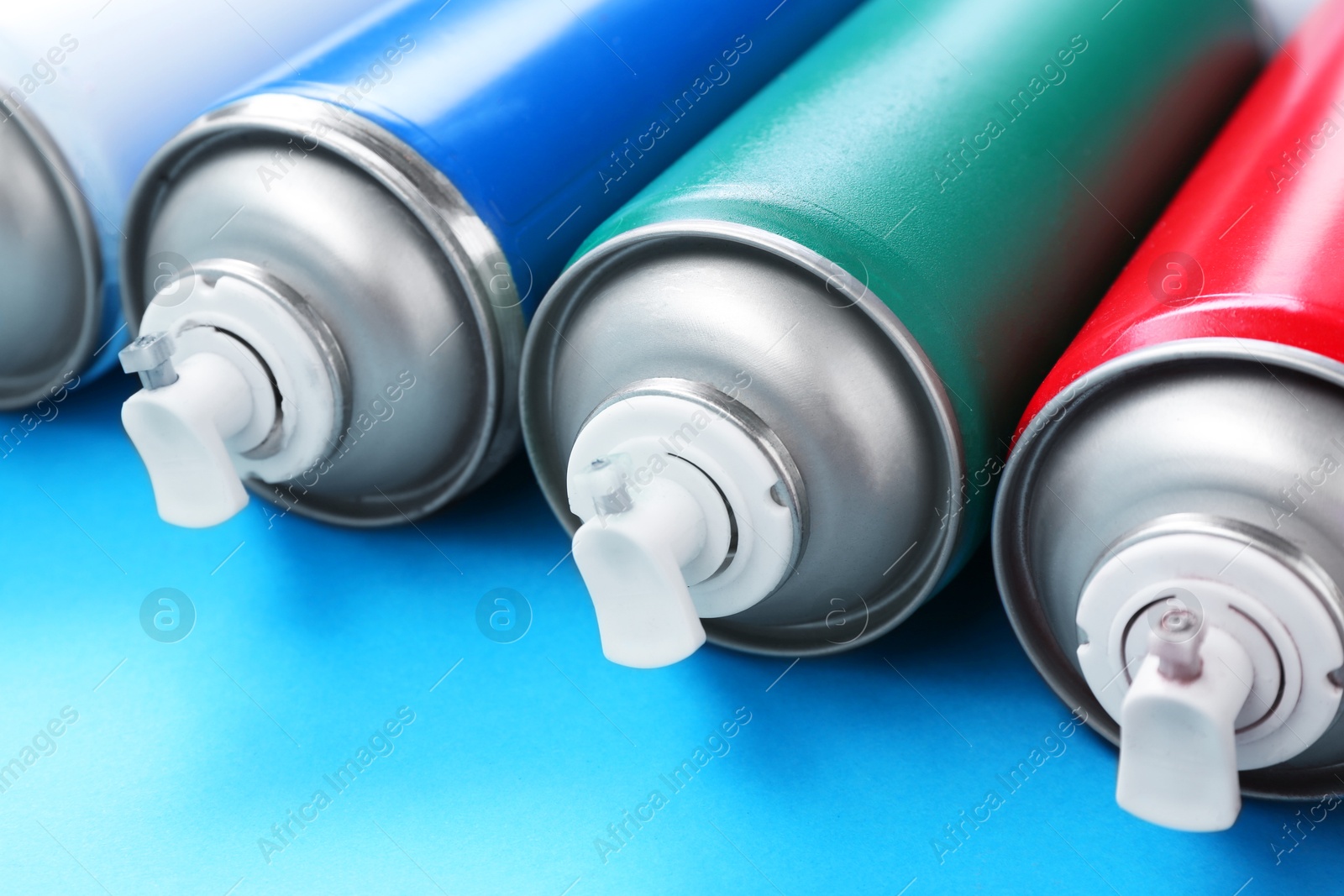 Photo of Many spray paint cans on light blue background, closeup