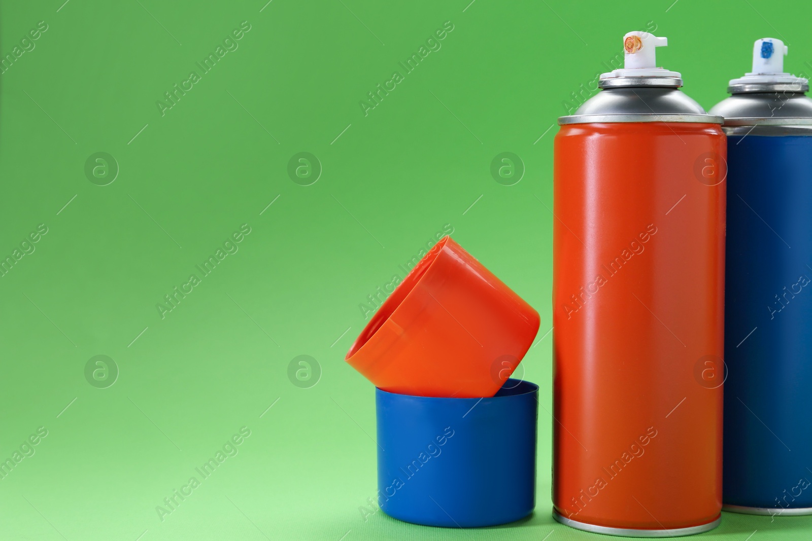 Photo of Two spray paint cans on green background, space for text