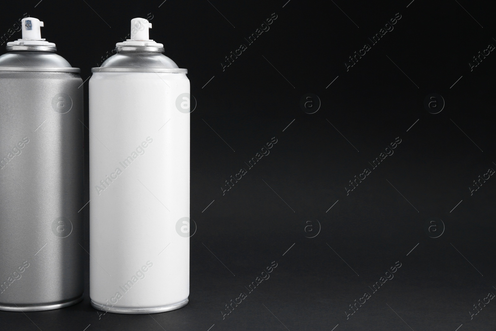 Photo of Two spray paint cans on dark gray background, space for text