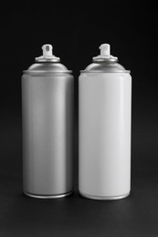 Two spray paint cans on dark gray background