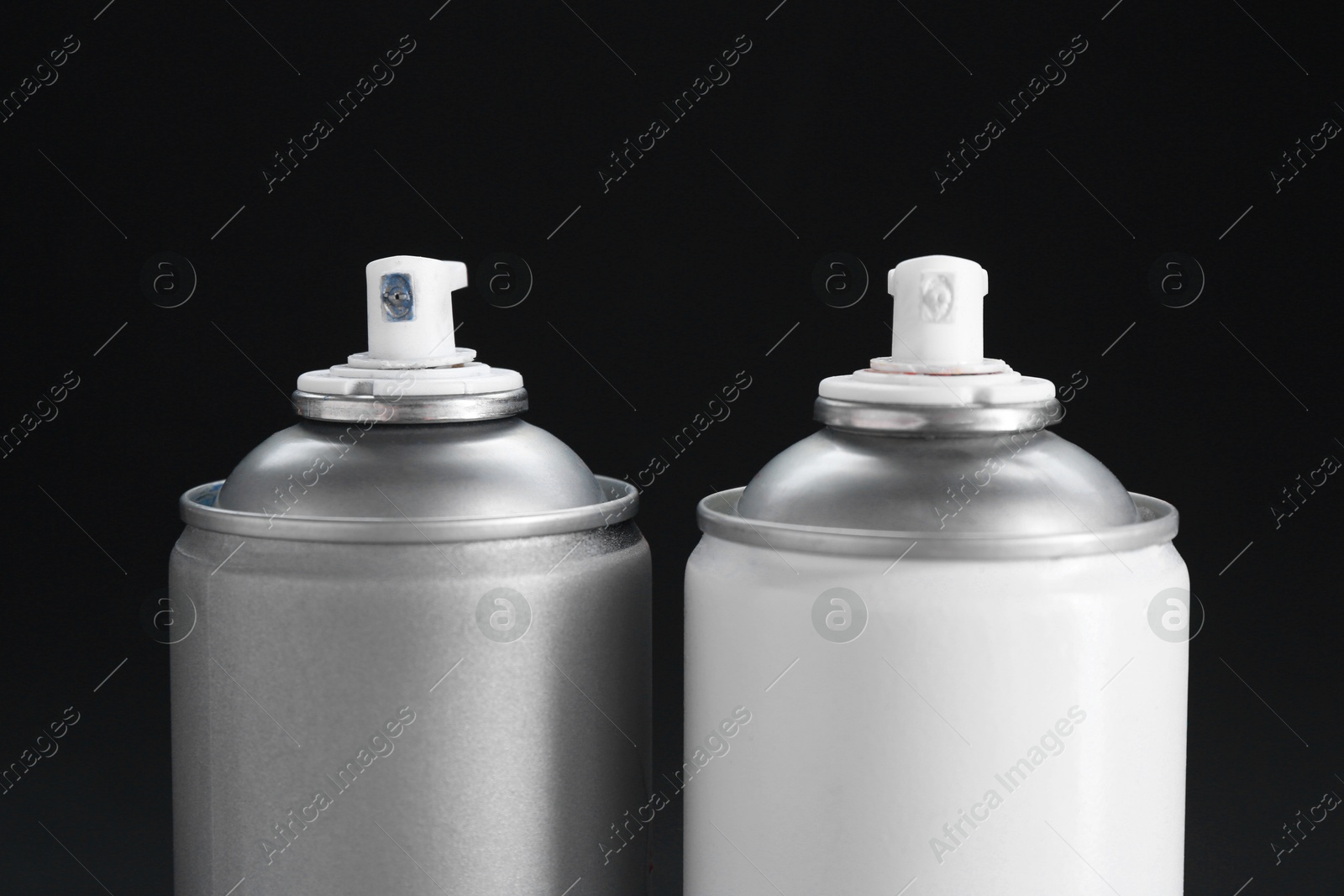 Photo of Two spray paint cans on dark gray background, closeup