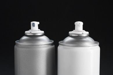 Two spray paint cans on dark gray background, closeup