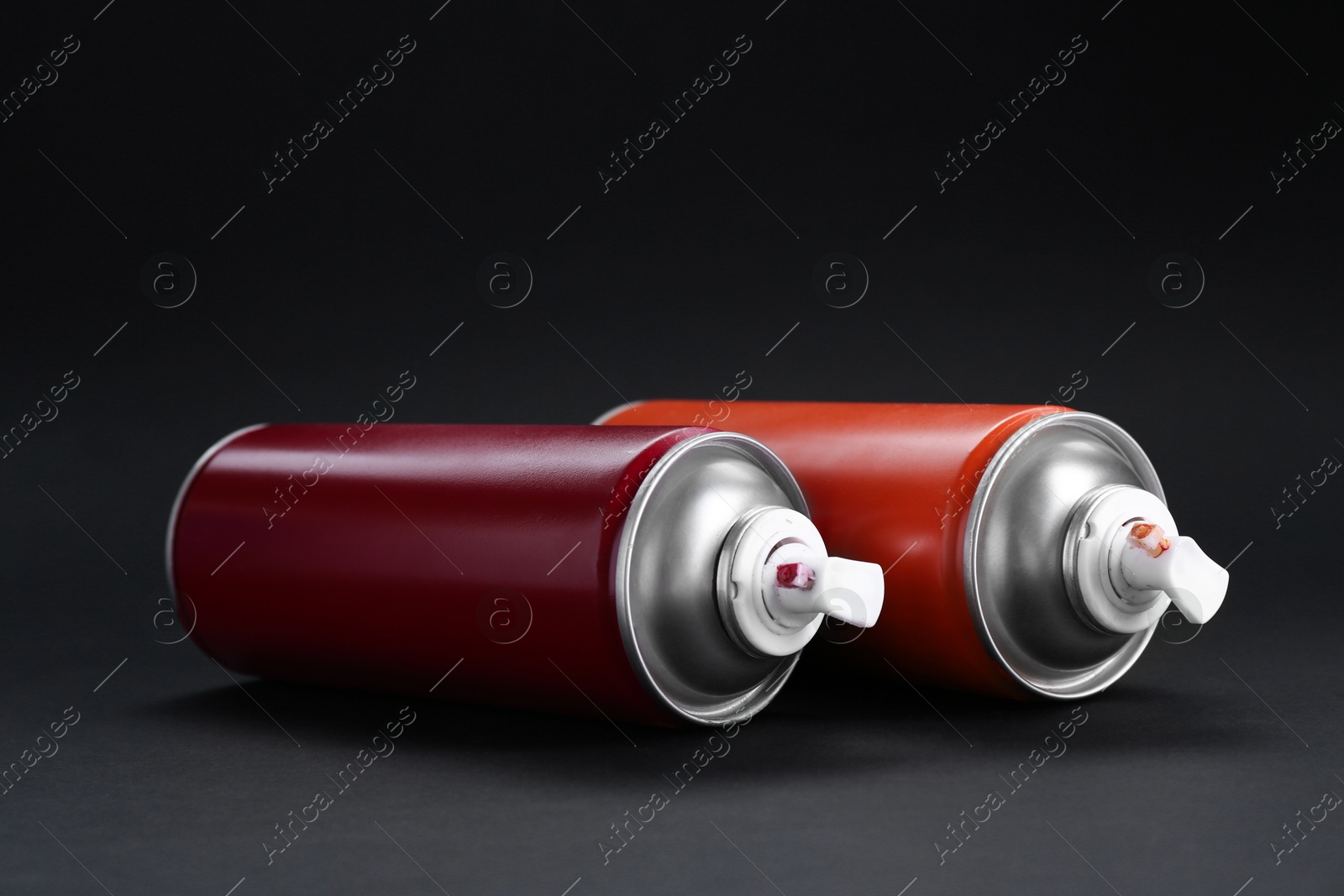 Photo of Two spray paint cans on dark gray background, closeup