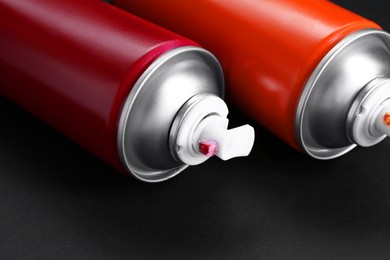 Two spray paint cans on dark gray background, closeup