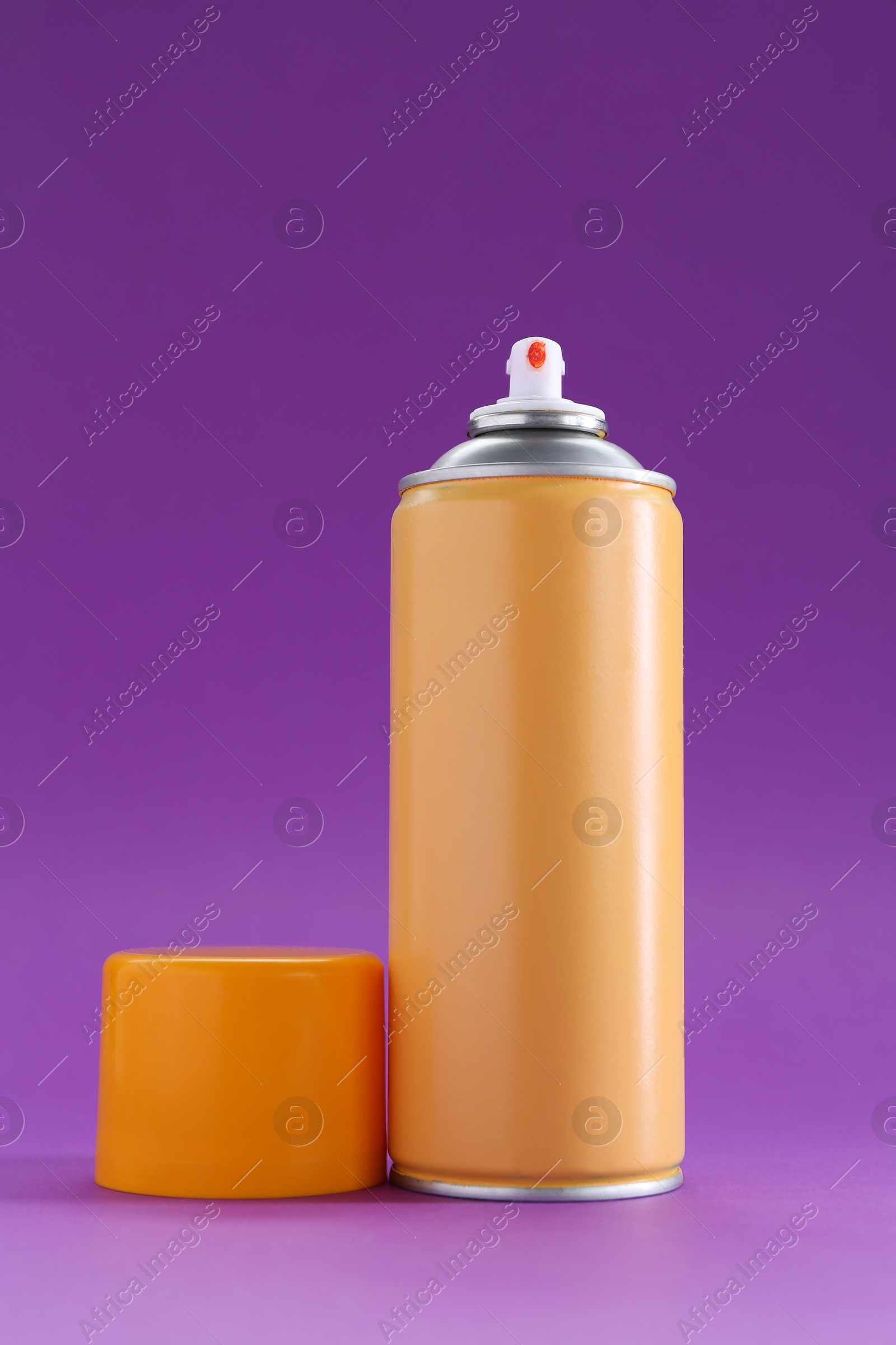 Photo of Orange spray paint can on violet background