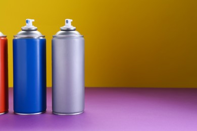 Many spray paint cans on color background, space for text