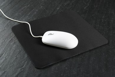 Photo of White wired mouse and mousepad on black textured table