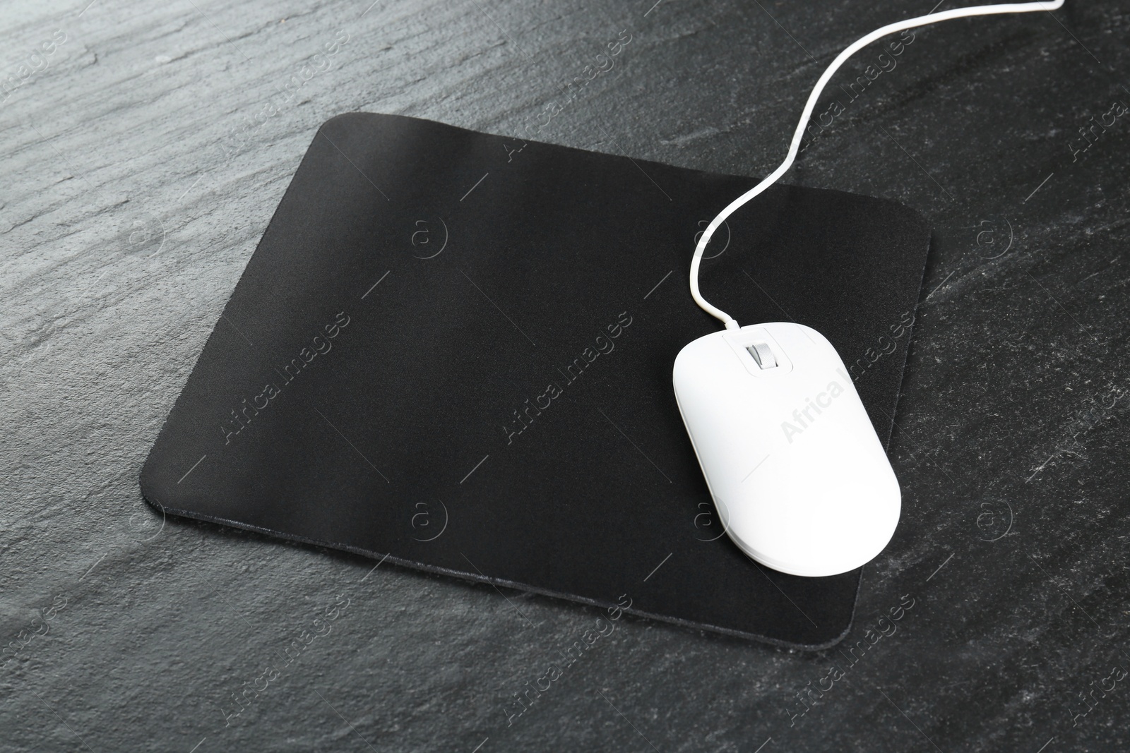 Photo of White wired mouse and mousepad on black textured table