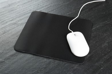 White wired mouse and mousepad on black textured table