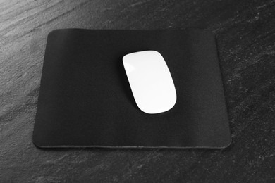 White wireless mouse and mousepad on black textured table