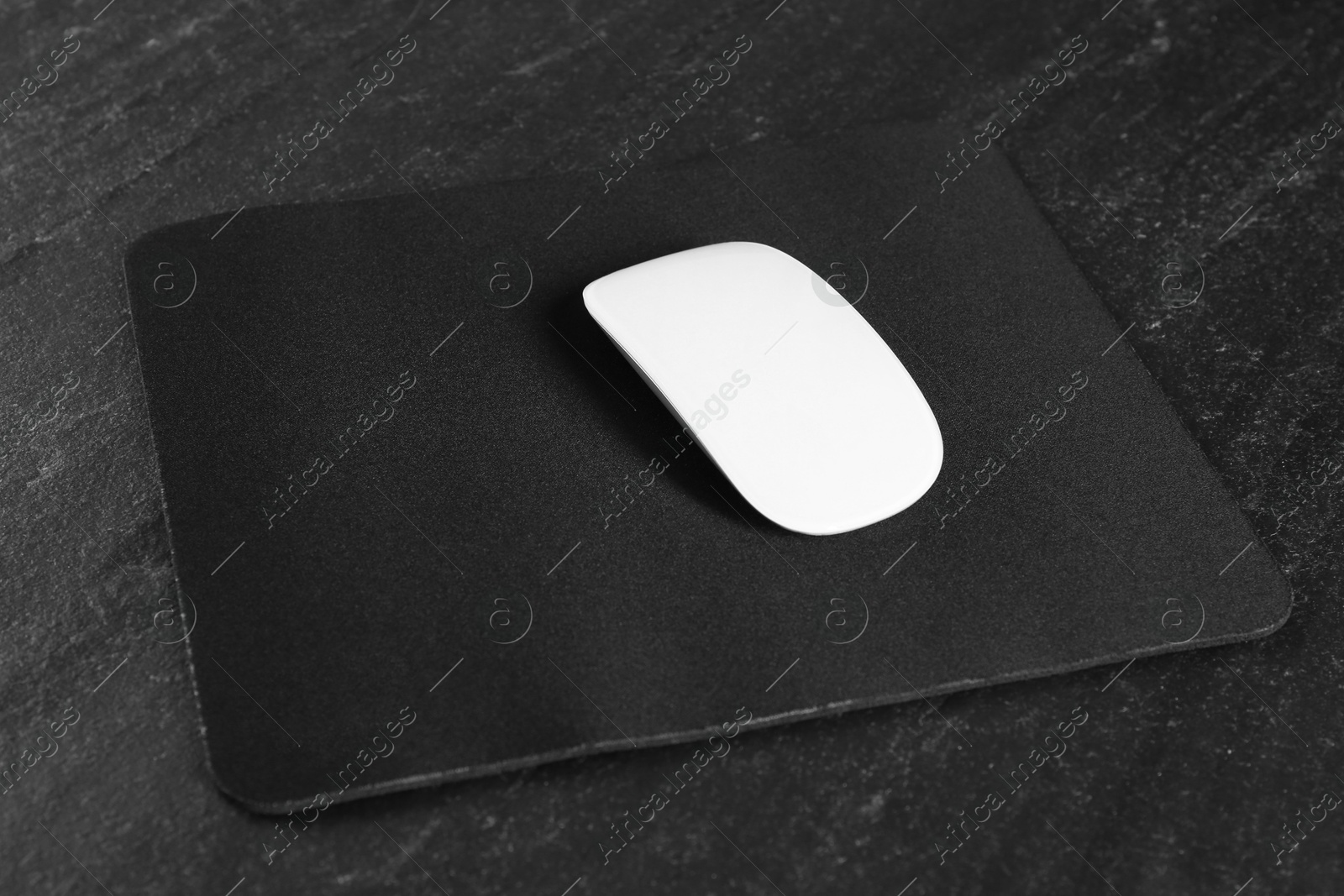 Photo of White wireless mouse and mousepad on black textured table