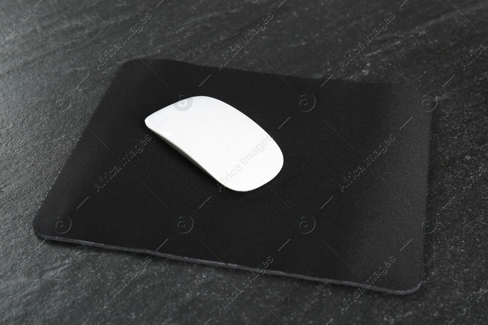 Photo of White wireless mouse and mousepad on black textured table