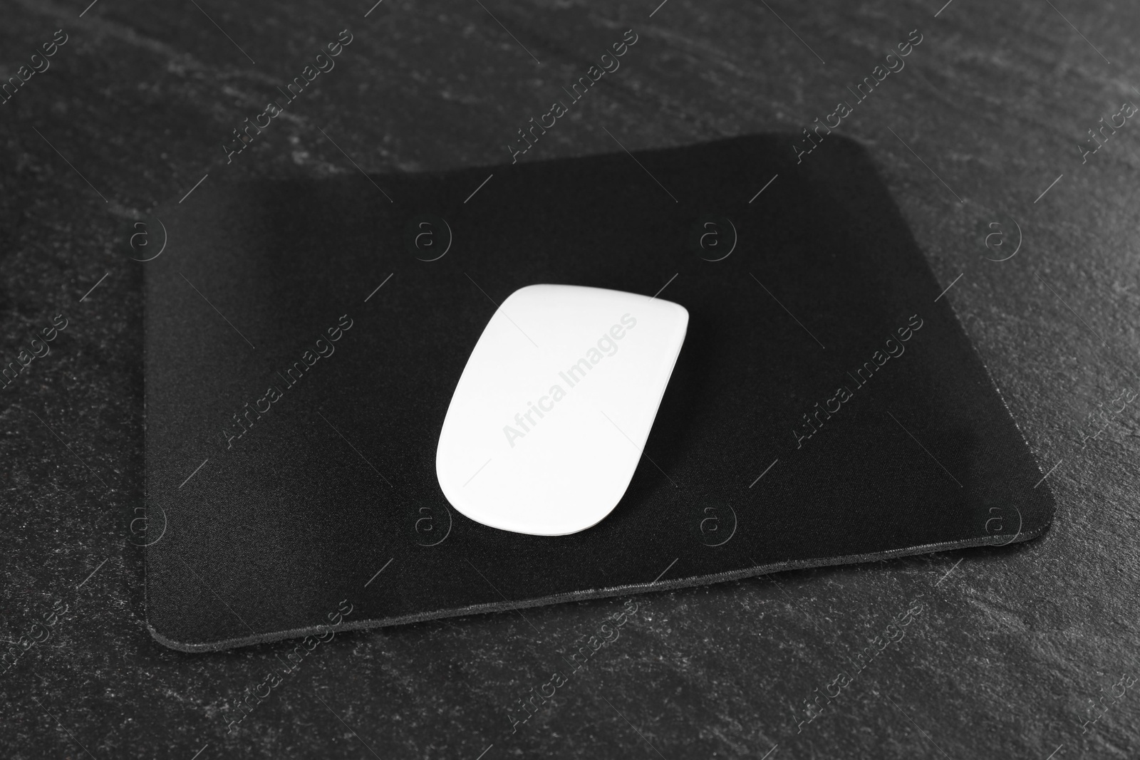 Photo of White wireless mouse and mousepad on black textured table