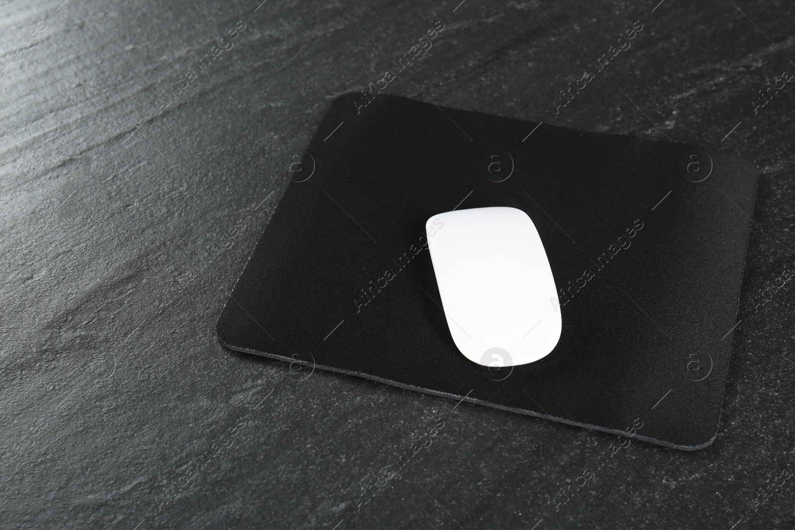 Photo of White wireless mouse and mousepad on black textured table