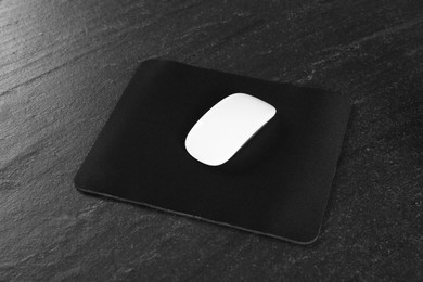 Photo of White wireless mouse and mousepad on black textured table