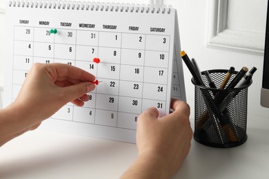 Photo of Timetable. Man marking date in calendar with drawing pins at white table, closeup