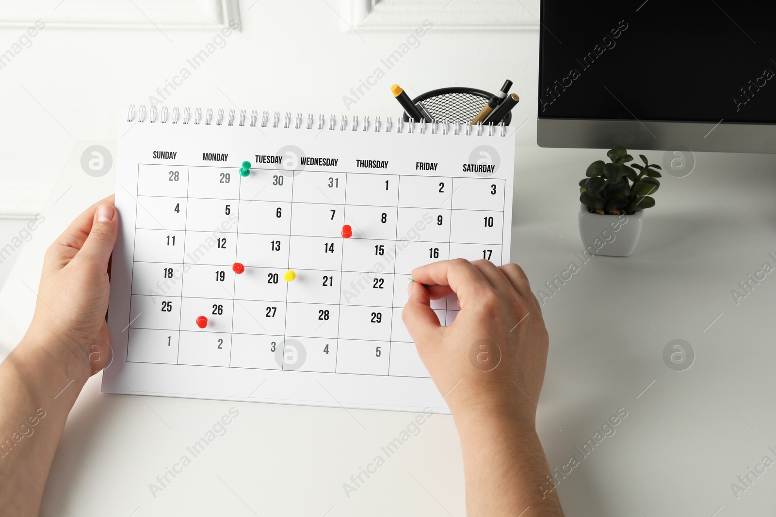 Photo of Timetable. Man marking date in calendar with drawing pins at white table, closeup