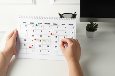 Photo of Timetable. Man marking date in calendar with drawing pins at white table, closeup