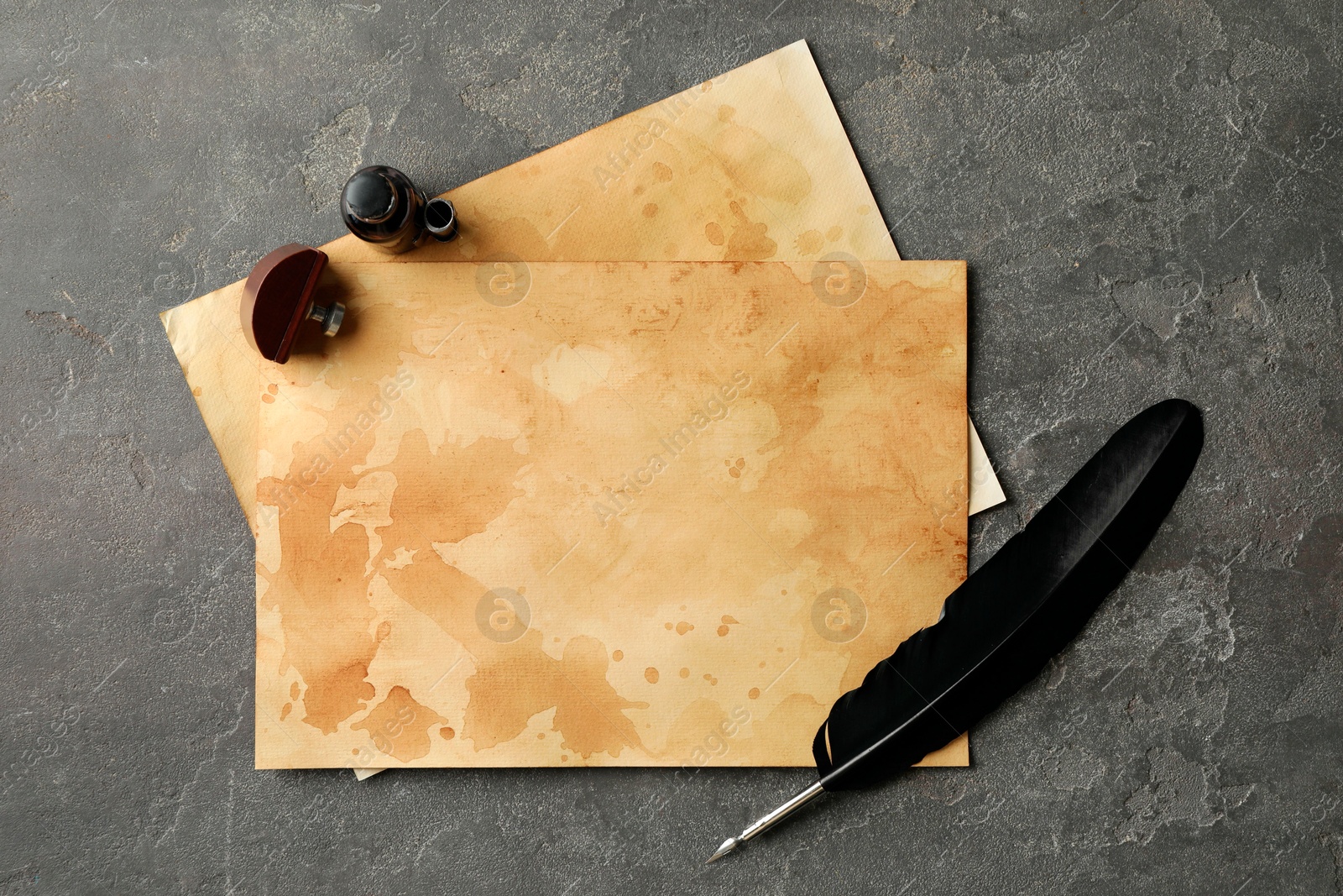 Photo of Black feather, inkwell and vintage parchment on grey table, flat lay