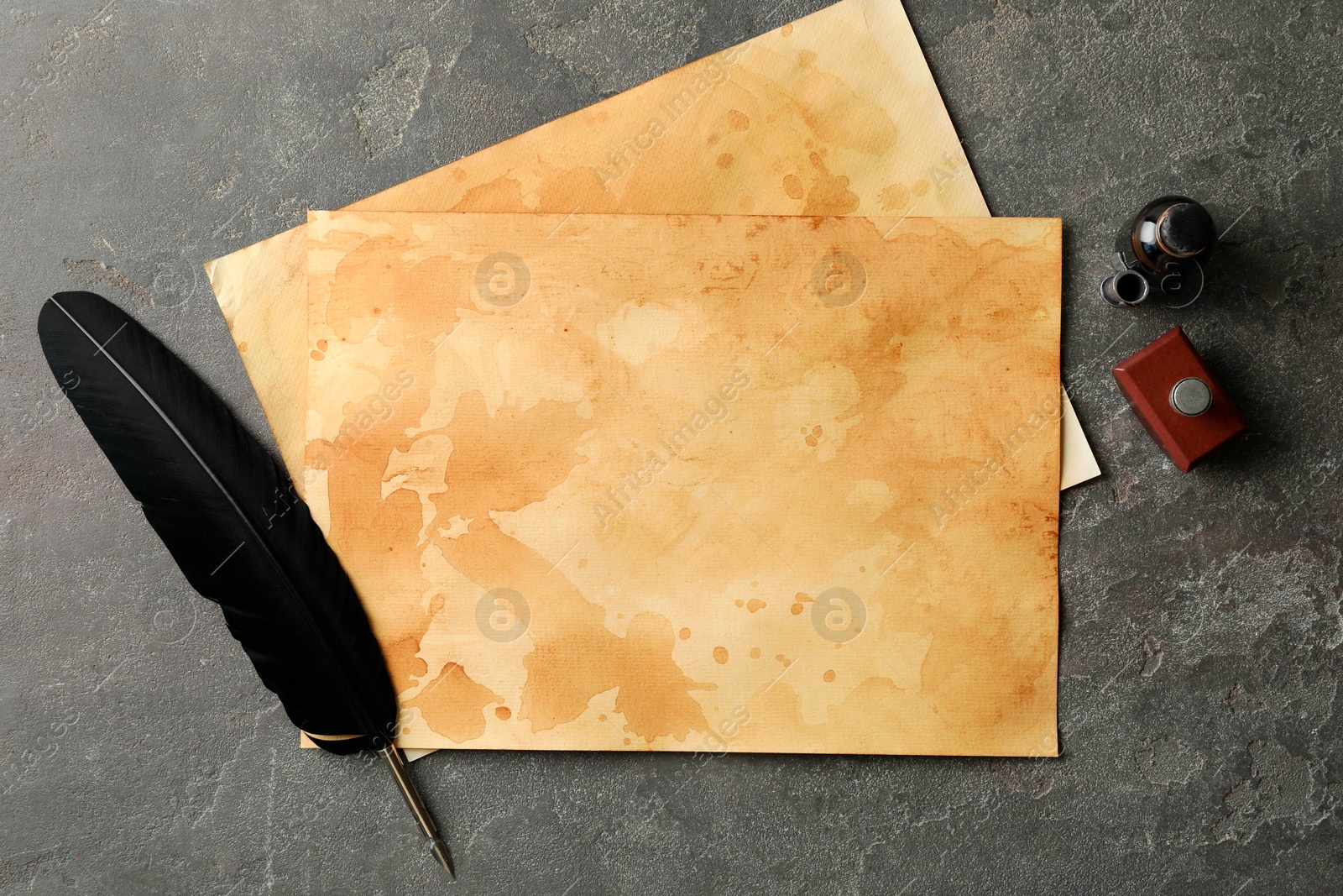 Photo of Black feather, inkwell and vintage parchment on grey table, flat lay