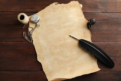 Sheet of old parchment paper, black feather, inkwell, rope and pocket chain clock on wooden table, flat lay