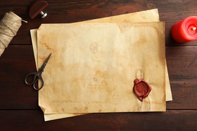 Photo of Sheet of old parchment paper with wax stamp, rope, scissors and candle on wooden table, flat lay