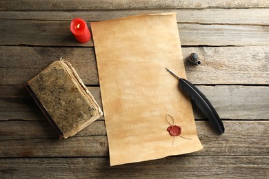 Sheet of old parchment paper with wax stamp, black feather, inkwell, vintage book and candle on wooden table, flat lay