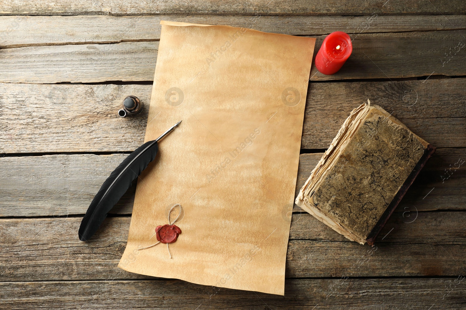 Photo of Sheet of old parchment paper with wax stamp, black feather, inkwell, vintage book and candle on wooden table, flat lay