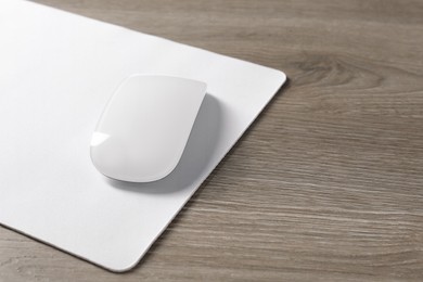 Wireless mouse and mousepad on wooden table, space for text