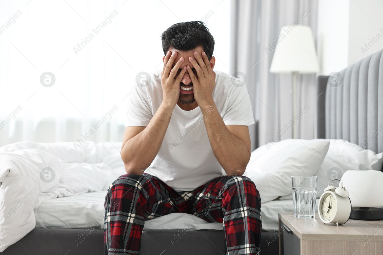 Photo of Tired man covering face with hands on bed at morning