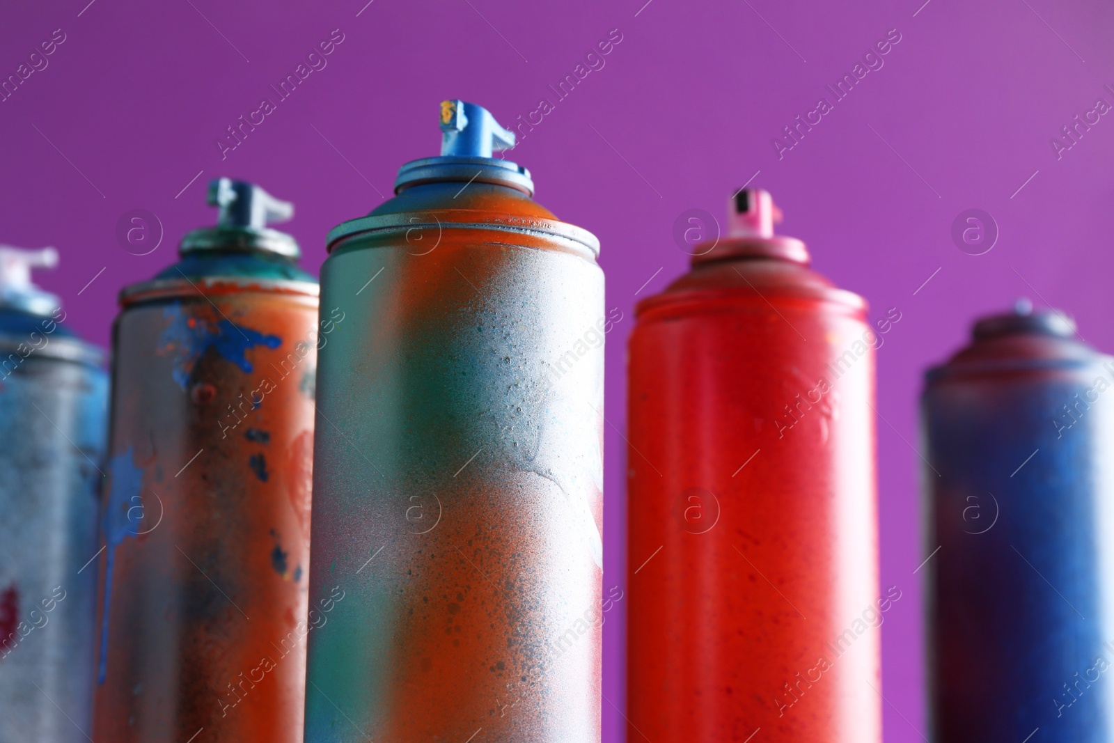 Photo of Many spray paint cans on violet background, closeup