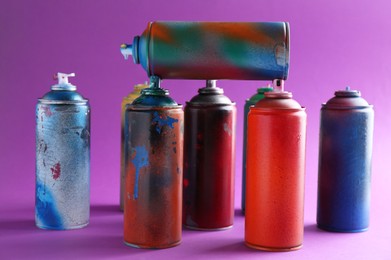 Photo of Many spray paint cans on violet background