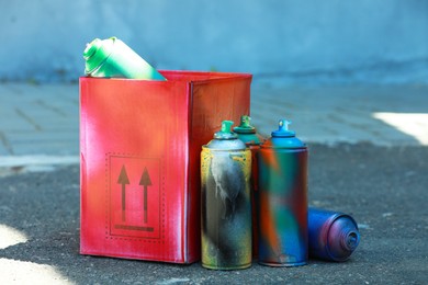 Many spray paint cans and red cardboard box outdoors