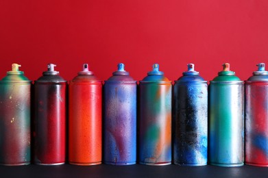 Many spray paint cans on black surface against red background