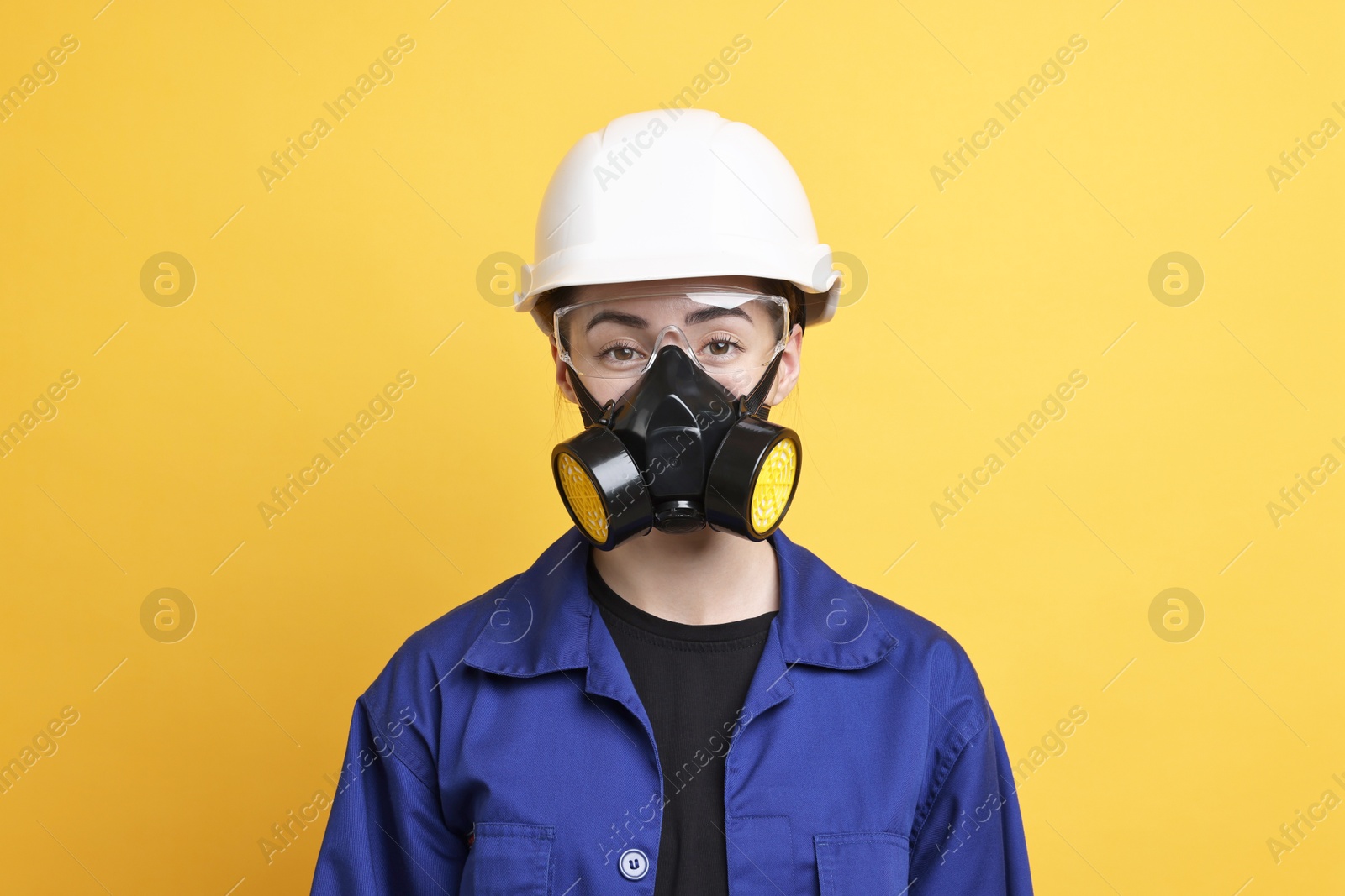 Photo of Worker in respirator, protective glasses and helmet on orange background