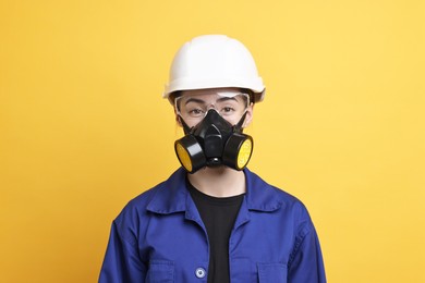 Worker in respirator, protective glasses and helmet on orange background