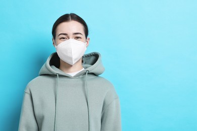 Woman in respirator mask on light blue background, space for text