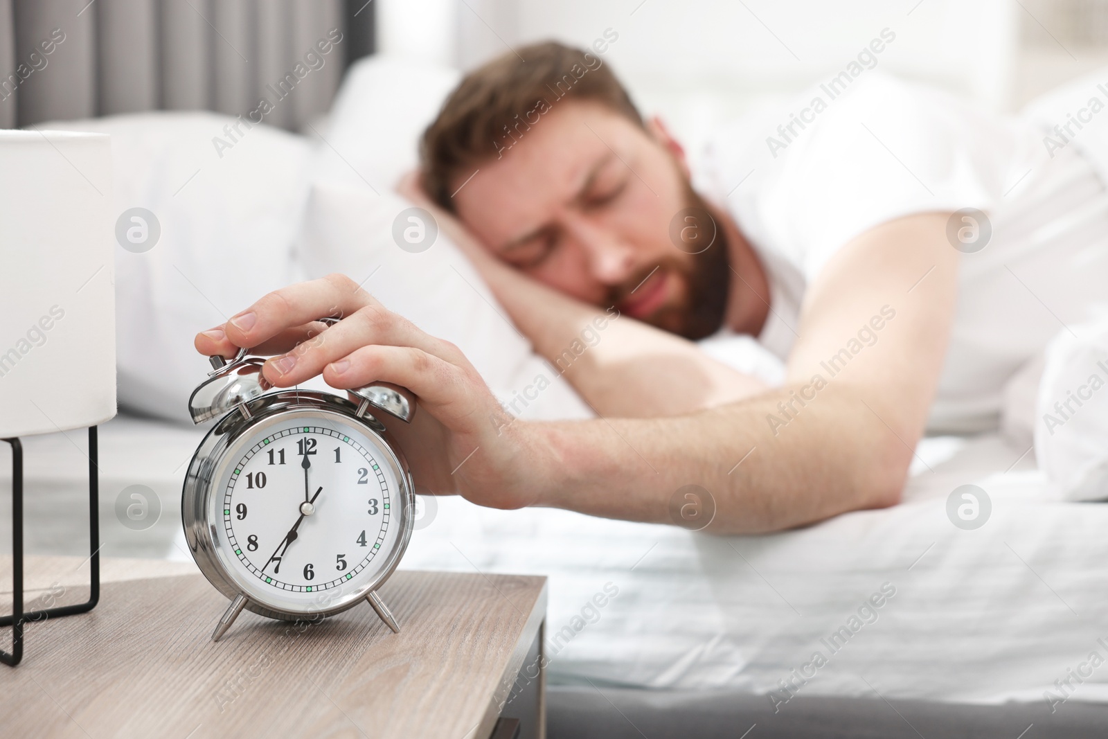 Photo of Sleepy young man turning off alarm clock in bedroom at morning, selective focus