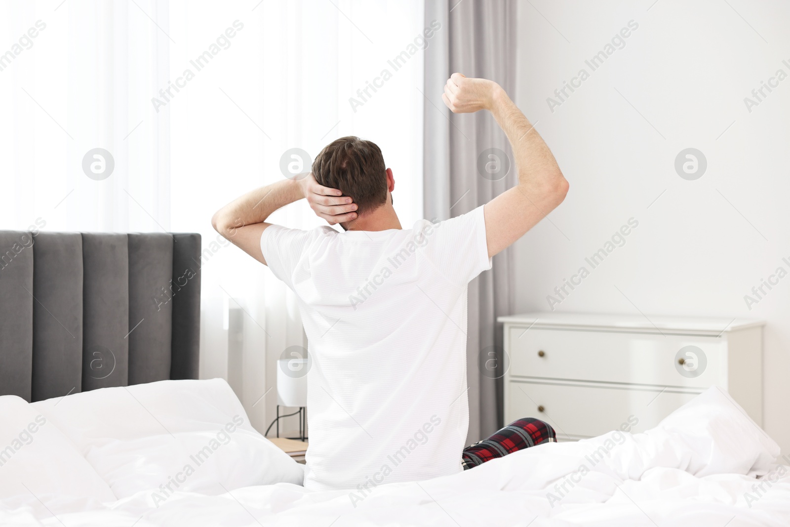 Photo of Young man stretching on bed at morning, back view