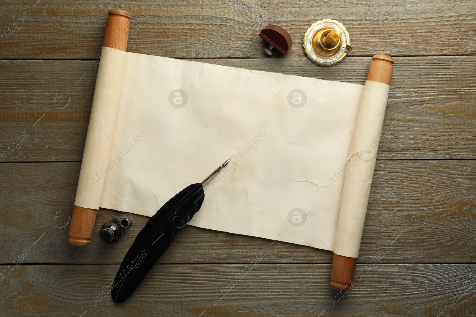 Photo of Sheet of old parchment paper, wax stamp, black feather, inkwell and candle on wooden table, top view