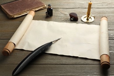 Photo of Sheet of old parchment paper, wax stamp, black feather, inkwell, candle and vintage book on wooden table