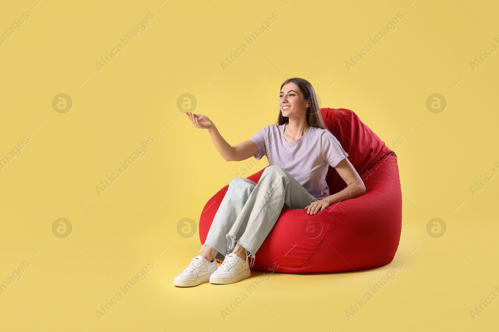 Photo of Smiling woman sitting on red bean bag chair against yellow background, space for text