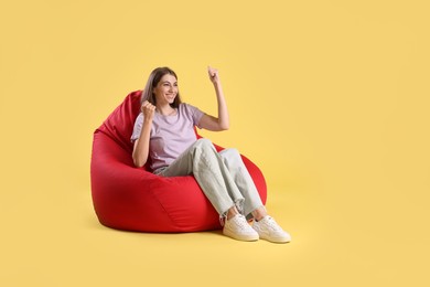 Photo of Smiling woman sitting on red bean bag chair against yellow background, space for text
