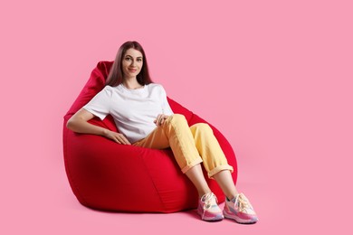 Photo of Beautiful young woman sitting on red bean bag chair against pink background